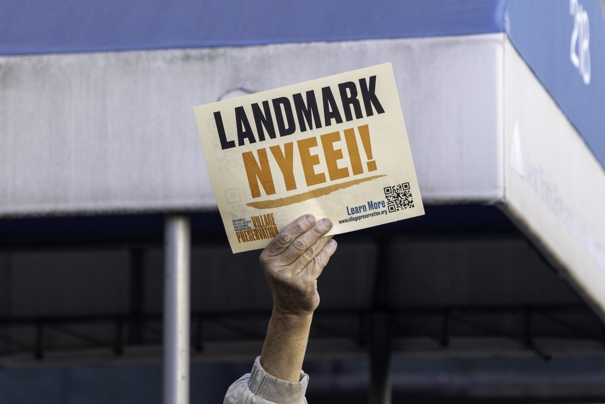 A hand holds a piece of paper up with the words “LANDMARK N.Y.E.E.I.!” written on it.