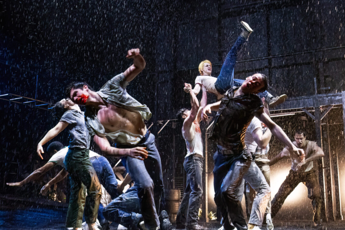 A bunch of men jumping on a stage in the rain, some having bloody faces.