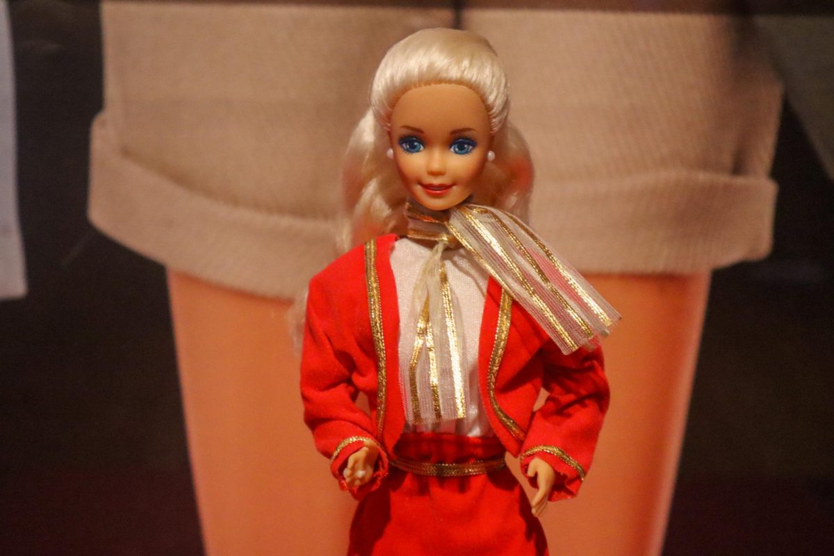 A blonde Barbie doll wearing a red jacket and gold necktie.