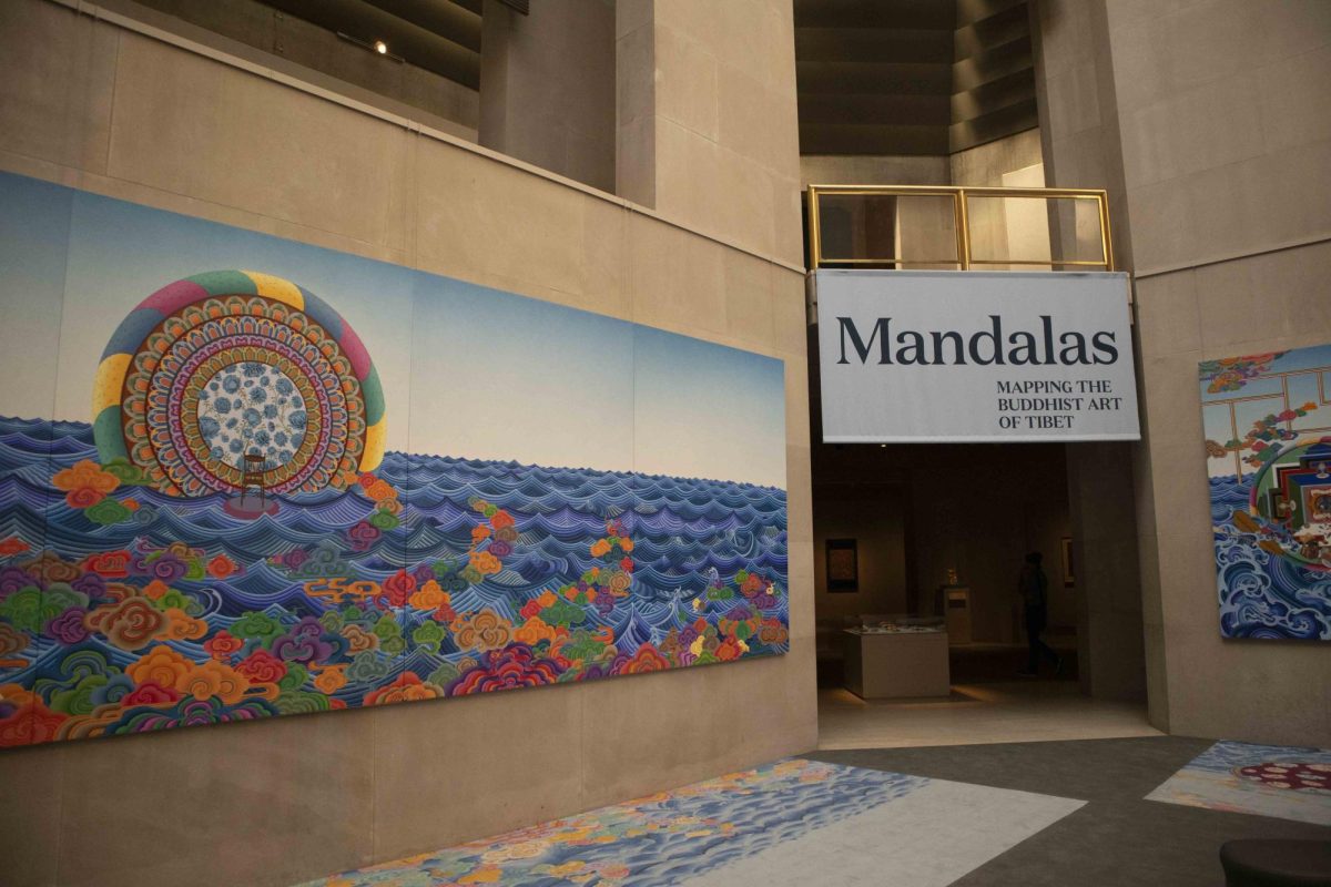 A colorful mosaic mandala on a wall next to a sign that reads “Mandalas Mapping the Buddhist Art”.