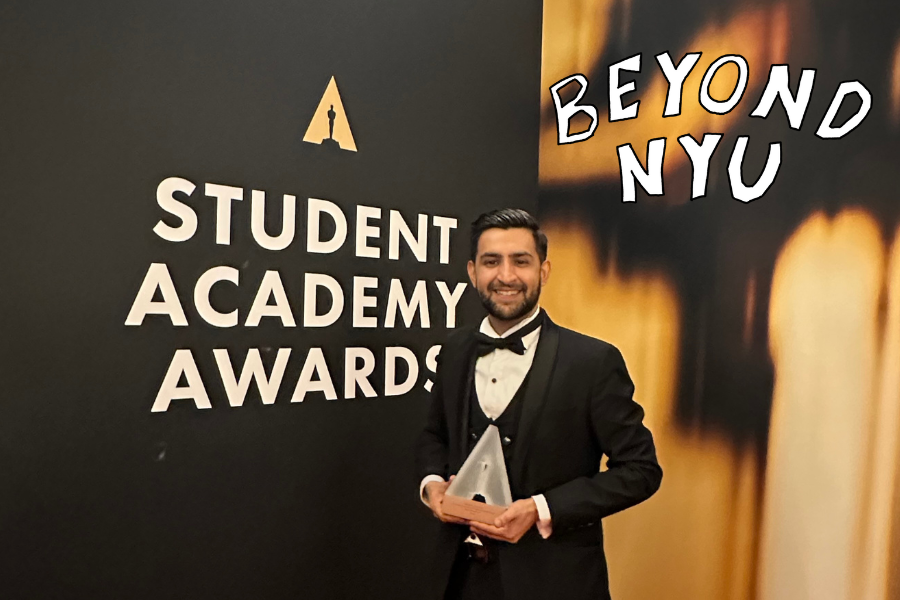 A man standing in a suit holding a trophy, with “STUDENT ACADEMY AWARDS” written on the wall behind him and “BEYOND NYU” written to the right.