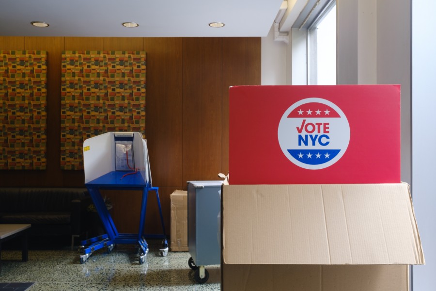 A red sign on top of a cardboard box reading “VOTE N.Y.C.” inside of a building.