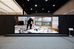 Image of a large screen with a man painting on the floor.