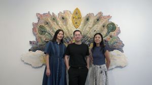 Three asian young people standing in front of an artwork.