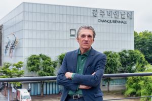 Portrait of a grey hair men with a blue jacked and green shirt in front of a museum.