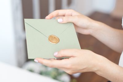 Close-up photo of female hands holding invitation envelope with a wax seal, a gift certificate, a postcard, wedding invitation card