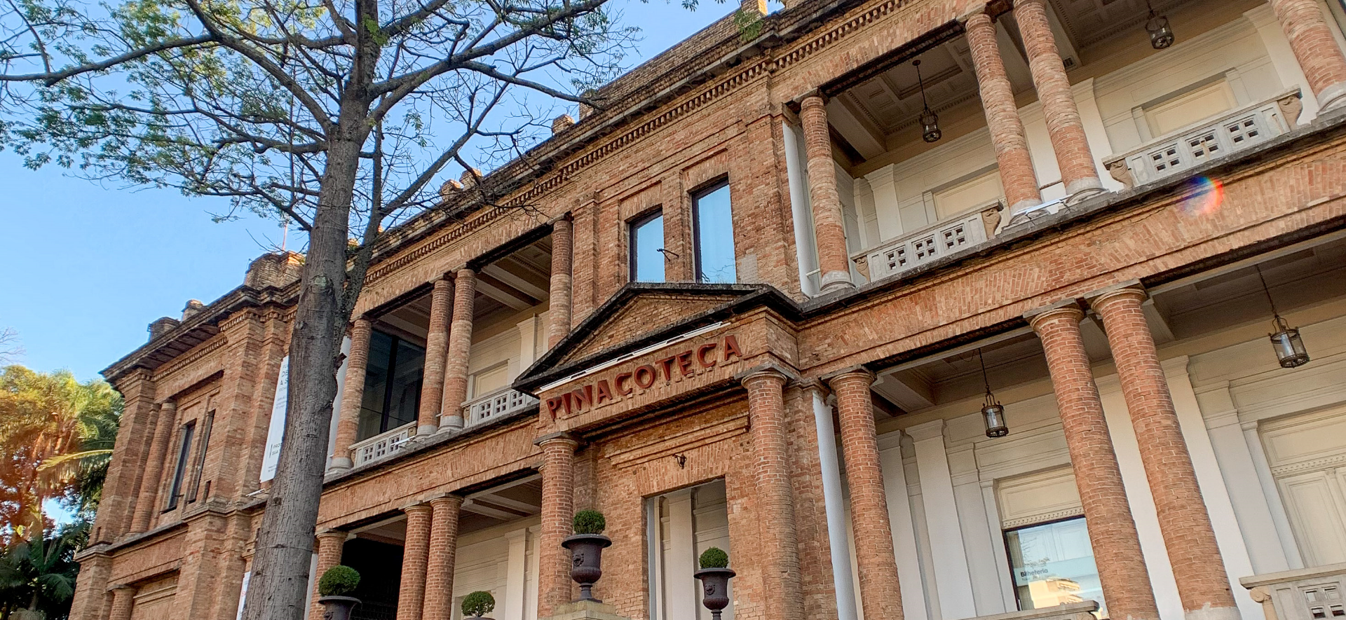 Foto da fachada da Pinacoteca durante o dia. Amplas pilastras e paredes em tijolos sem revestimento.