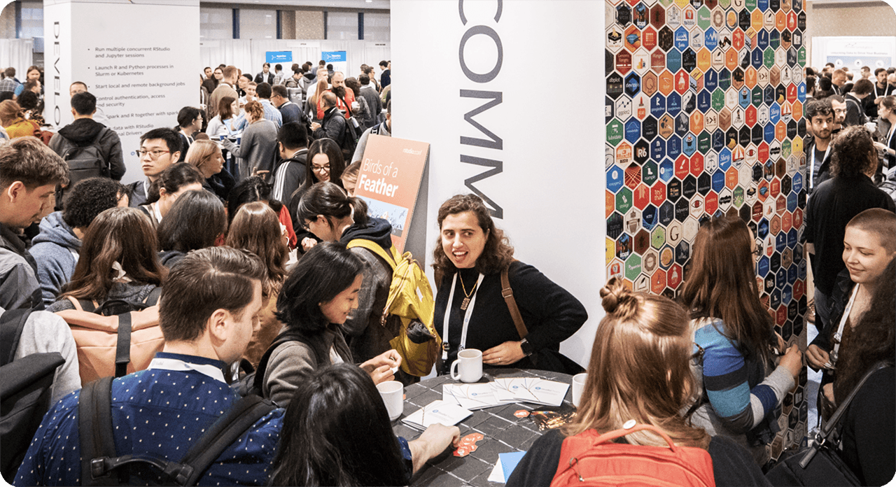 Large group of people in a conference space around columns with 'Community' text graphics and a tessellation of hex stickers