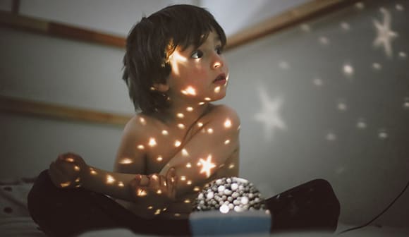 a young boy in a darkened room looks at stars projected on the wall