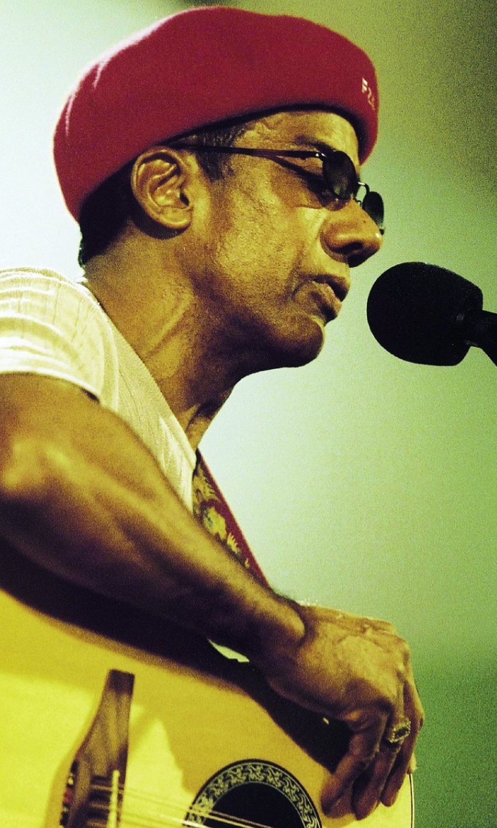 Jorge Ben Jor toca violão e canta com oculos escuros e boina vermelho