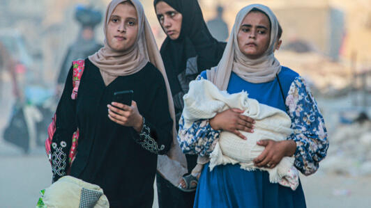 A woman holds a baby wrapped in a blanket as displaced Palestinians leave an area in Khan Younis after the Israeli army issued a new evacuation order.
