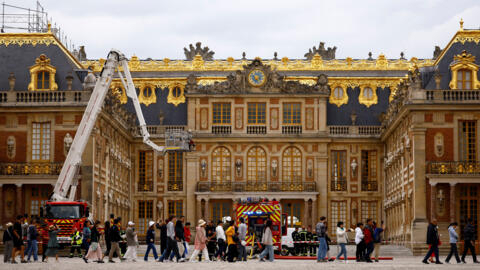 Visitors walk past as French firefighters work after a fire broke out at the Chateau de Versailles forcing the site's evacuation, but was swiftly brought under control, in Versailles, near Paris, Fran