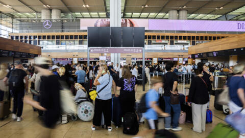 Passengers wait in front of a blank display board at Brandenburg Airport in Berlin, Germany, on Friday, July 19, 2024, after a widespread computer failure that disrupted flights, banks, media and busi