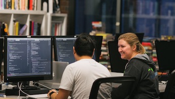 A female and male engineer programming together at a coworking desk