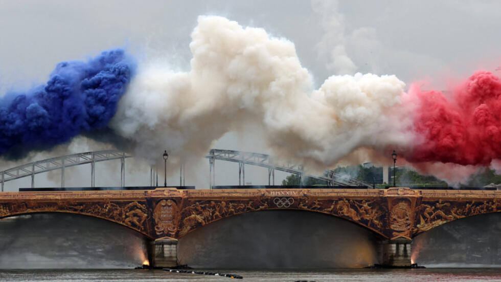 سحابة دخان ضخمة بالأزرق والأبيض والأحمر تمثل ألوان العلم الفرنسي ترتفع أعلى جسر فوق نهر السين بداية حفل الافتتاح