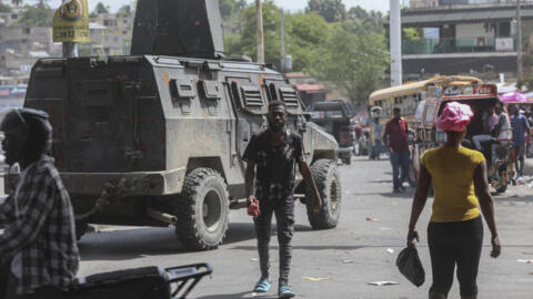 People walk past an armored police vehicle patrolling the streets in Port-au-Prince, Haiti, on 15 July, 2024.