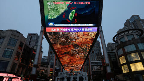 A large screen shows news footage of a map of military drills conducted by the Eastern Theatre Command of the Chinese People's Liberation Army (PLA) in five areas around the island of Taiwan, in Beiji