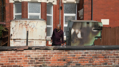 A man inspects damaged clothing bins and a fence of the Southport Islamic Society Mosque, after a violent protest, following a vigil for victims of the knife attack in Southport, Britain July 31, 2024