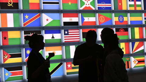 People stand in front of a screen featuring flags of countries taking part in the Forum on China-Africa Cooperation at the National Convention Centre in Beijing in September, 2024.