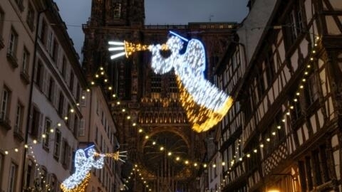 Pessoas caminham sob decorações de Natal com a Catedral de Estrasburgo ao fundo enquanto participam do dia de abertura do tradicional mercado de Natal, em Estrasburgo, nordeste da França, em 24 de novembro de 2023. (Foto de PATRICK HERTZOG / AFP)