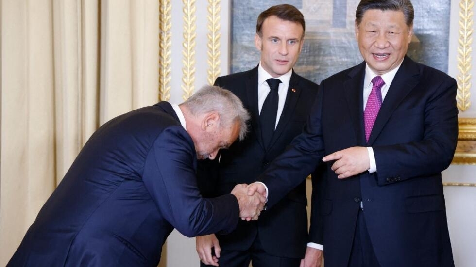 中國國家主席對法國進行為期兩天的國事訪問期間，法國電影製片人呂克·貝松（左）在正式國宴前的演講中與中國國家主席習近平（右）握手，法國總統馬克龍（中）在場。  2024 年5 6日 巴黎愛麗舍宮 
