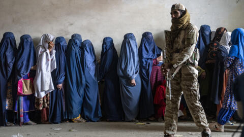 Un combatiente talibán monta guardia mientras unas mujeres esperan para recibir raciones de comida distribuidas por un grupo de ayuda humanitaria, en Kabul, Afganistán, el 23 de mayo de 2023.