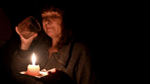 Foto de uma mulher ucraniana durante um apagão usando uma vela. Desde outubro, as infraestruturas elétricas da Ucrânia sofrem ataques russos, deixando os habitantes do país no escuro. 