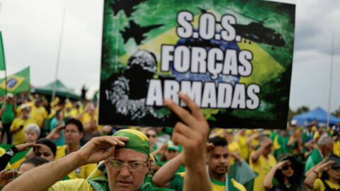 Um homem segura uma placa que diz "SOS Forças Armadas" durante um protesto realizado por apoiadores do presidente Jair Bolsonaro contra o presidente eleito Luiz Inácio Lula da Silva, na sede do Exército em Brasília, Brasil, em 7 de novembro de 2022.