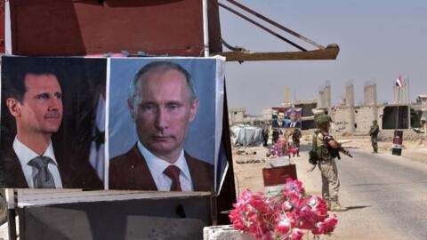 Russian and Syrian troops stand guard near posters of Syrian President Bashar al-Assad and Russia's Vladimir Putin at the Abu Duhur crossing on the eastern edge of Idlib province