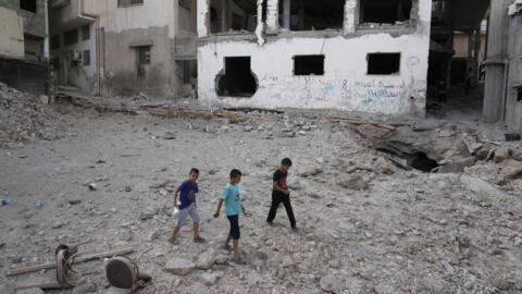 Meninos palestinos caminham sobre os escombros no oeste de Jenin, horas depois de militares israelenses deixarem a cidade, na madrugada desta sexta-feira (6).