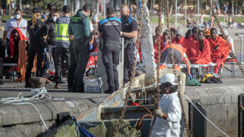 Migrants sit on the pier of Los Cristianos port following their rescue by the Spanish Sea Search and Rescue agency vessel "Salvamar Alpheratz" off the coast of the Canary Island of Tenerife, on 2 February, 2024.