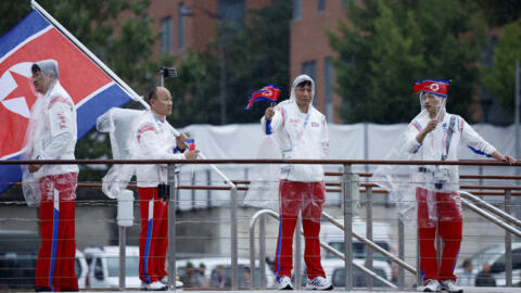 Les athlètes de la délégation de la Corée du Nord brandissent des drapeaux à bord d'un bateau lors du défilé flottant sur la Seine lors de la cérémonie d'ouverture des Jeux olympiques, le 26 juillet 2024.