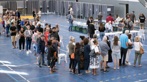 People queue in front of polling stations inside the Anse Vata sports hall to vote in the first round of France's crunch legislative elections in Noumea, in France's Pacific territory of New Caledonia