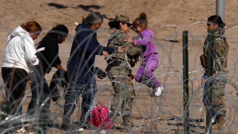 Una agente de la Guardia Nacional de Texas levanta a una niña migrante por encima de una valla de púas a orillas del Río Grande en El Paso, estado de Texas, en la frontera con México, el 30 de enero de 2024.
