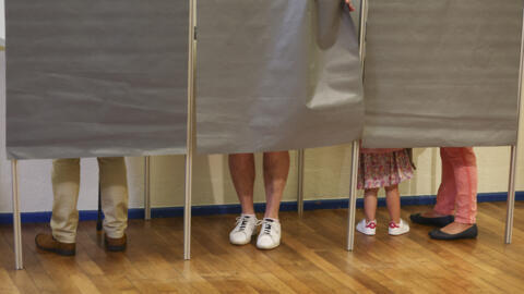 People stand in voting booths to vote in the first round of the early French parliamentary elections, at a polling station in Tulle, France, June 30, 2024.