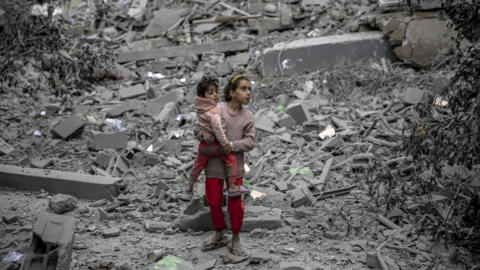 A Palestinian girl carries a child through the rubble of houses destroyed by Israeli bombardment in Gaza City on 3 March, 2024.