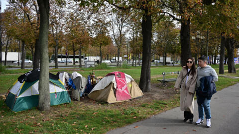 Passers-by walk past tents of homeless people near the Seine river in central Paris, on 18 October 2023.