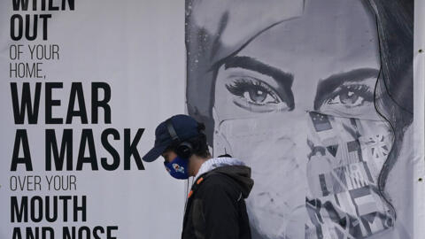 Homem passa diante de um cartaz em São Francisco, Estados Unidos, onde está escrito "use máscara". 