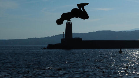 A youth is silhouetted as he dives into the Mediterranean sea on the French riviera city of Nice, on 11 August 2024.