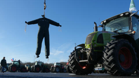 An effigy of a farmer in overalls hangs near tractors belonging to protesting farmers blocading the A10 autoroute during a protest southwest of Paris, on 26 January, 2024.