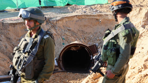 2023年12月15日，在以色列军队组织的一次媒体访问期间拍摄的这张照片中，士兵们站在一条地道的入口处。