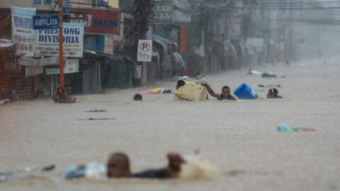 Des personnes tentent de traverser une route inondée à cause du typhon Gaemi, à Marikina aux Philippines, le 24 juillet 2024.