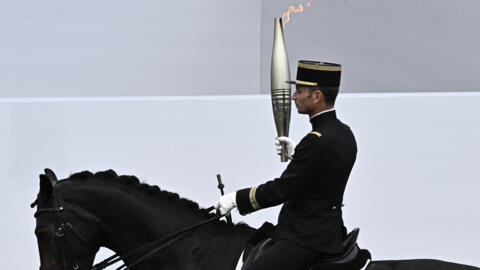 O chefe dos escudeiros do Cadre Noir de Saumur e medalhista de ouro no Rio em 2016, Thibaut Vallette, segura a tocha da chama olímpica durante o desfile militar do Dia da Bastilha ao longo da Avenida Foch, em Paris, em 14 de julho de 2024.