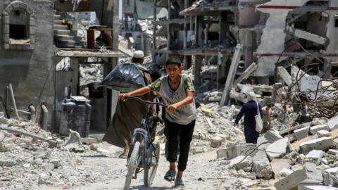 Un Palestinien pousse un vélo alors qu'il passe devant les décombres de maisons détruites par des bombardements israéliennes, à Khan Younès, dans le sud de la bande de Gaza, le 10 juillet 2024.