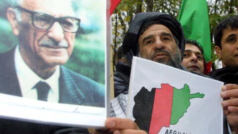 An Afghan refugee, supporter of former Afghan kind Mohammad Zahir Shah (portrait at L) demonstrates 27 November 2001, outside the Petersberg hotel in Koenigswinter.  A nine-member delegation of former