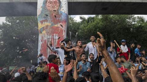 Protesters celebrate beside a defaced portrait of Prime Minister Sheikh Hasina after news of her resignation, in Dhaka, Bangladesh, Monday, Aug. 5, 2024. (