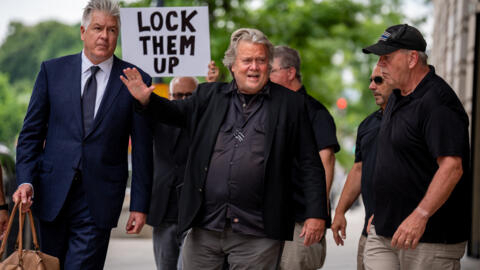Un homme brandit une pancarte «Enfermez-les», alors que Steve Bannon quitte le tribunal fédéral de Washington, le 6 juin 2024.