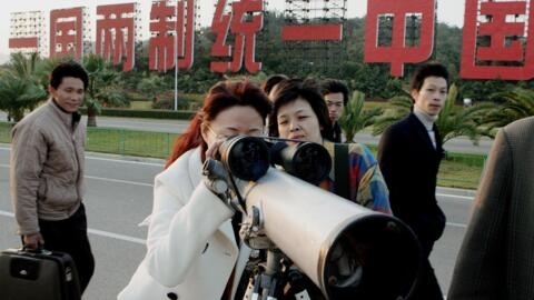 Photo d'archive montrant des Chinois observant, depuis le continent, l'île taiwanaise de Kinmen en 2005. Derrière, en grosses lettres : «Un pays, deux systèmes, unifiez la Chine»