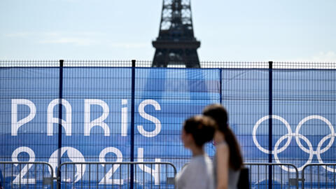 Turistas passam diante de barreira que esconde a Torre Eiffel, nesta sexta-feira, 19 de julho de 2024, a uma semana da cerimônia de abertura dos Jogos Olímpicos.