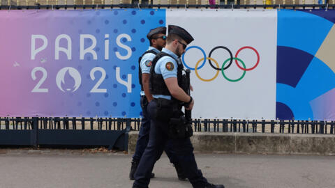Police patrol in front of the Assemblée Nationale passing an advertising poster of the Paris 2024 Olympic Games.